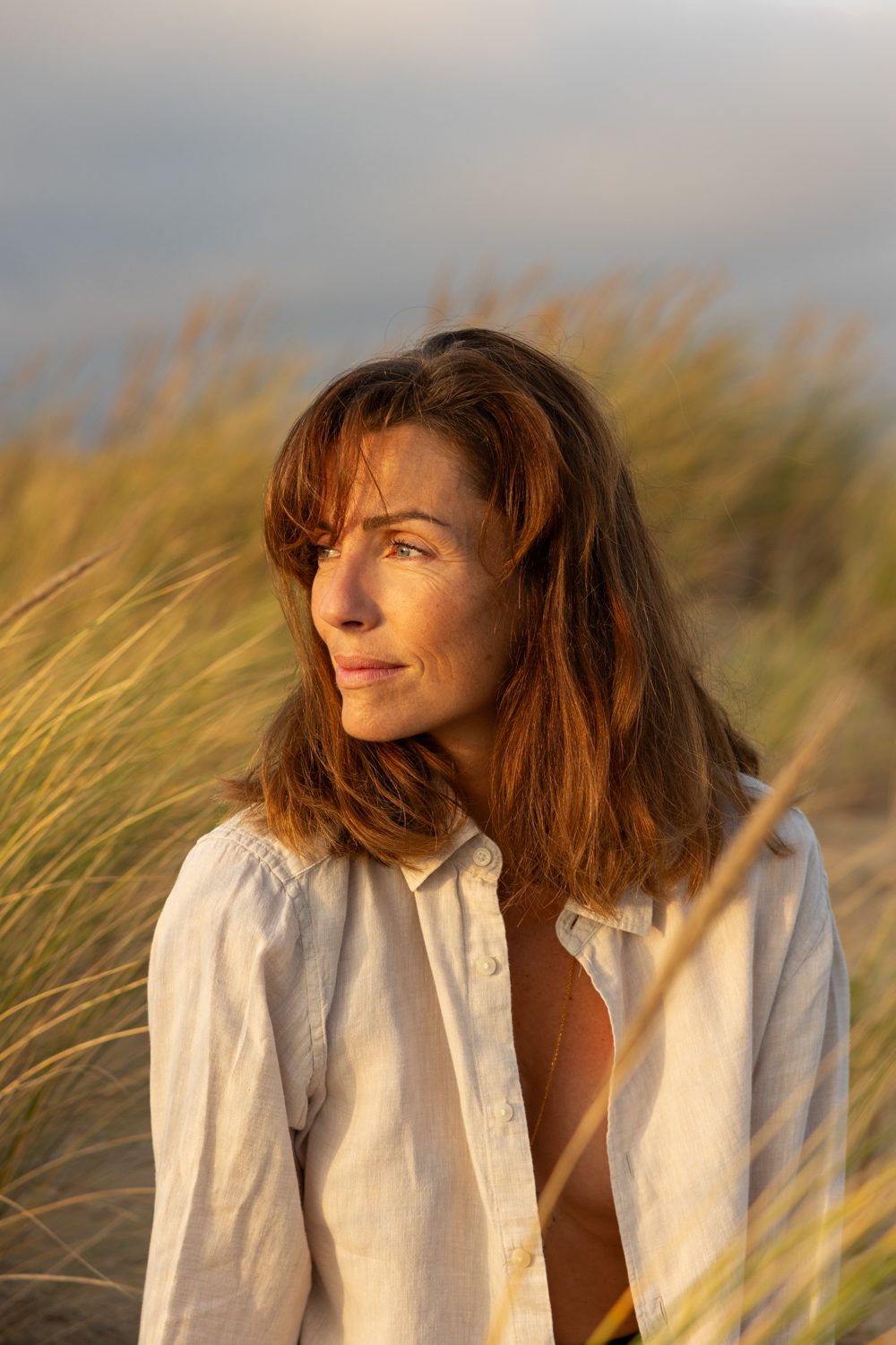 Femme assise dans les dunes, regard vers la droite