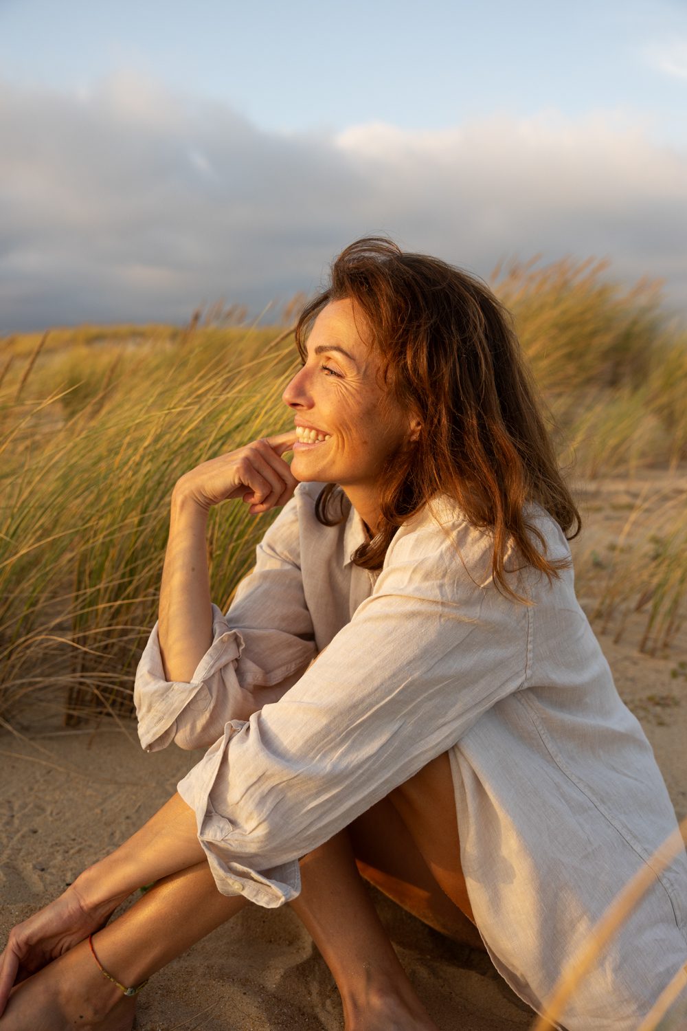 Femme assise dans les dunes souriant main près du visage