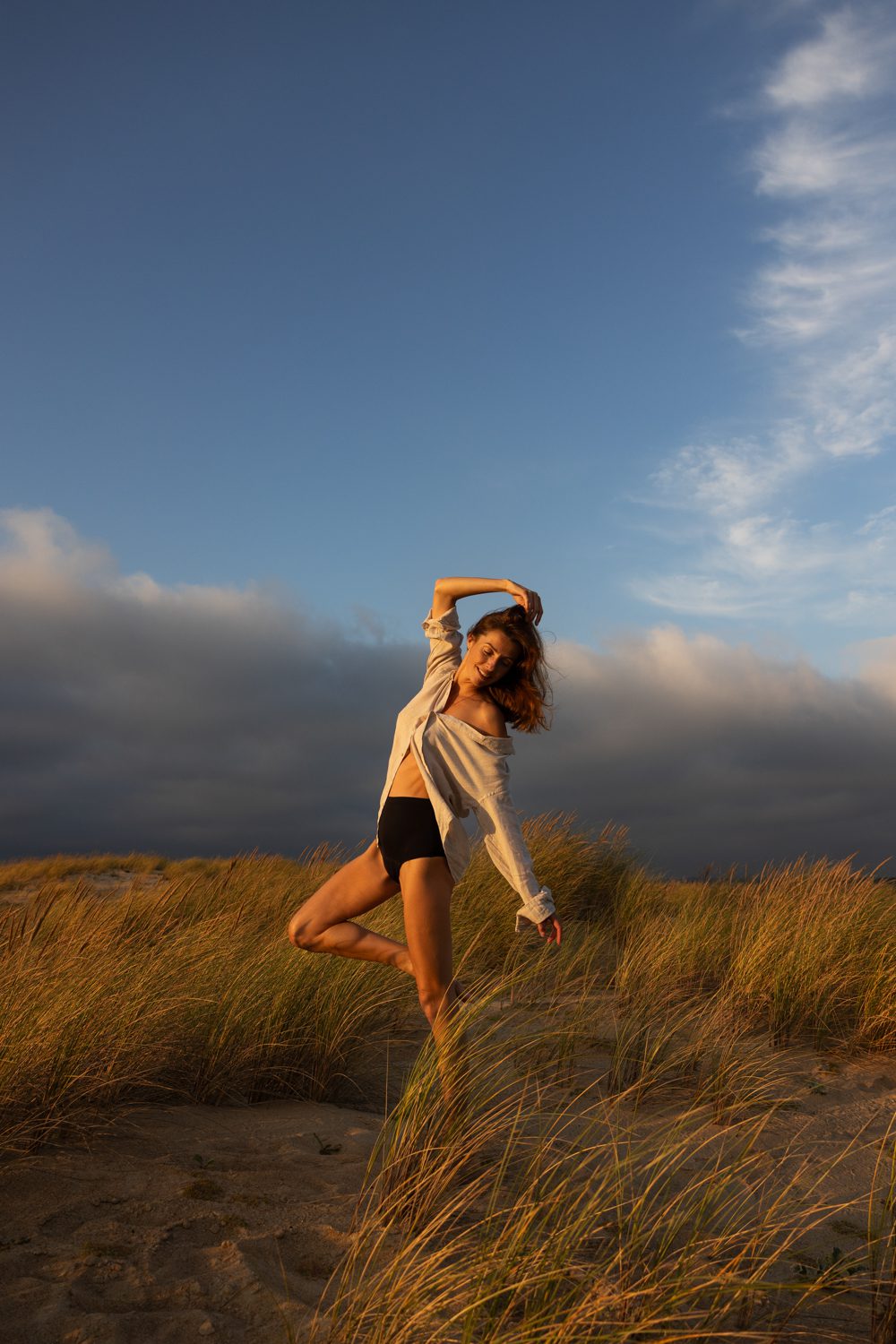 Femme debout dans les dunes, vêtue de clair, regard vers l’horizon