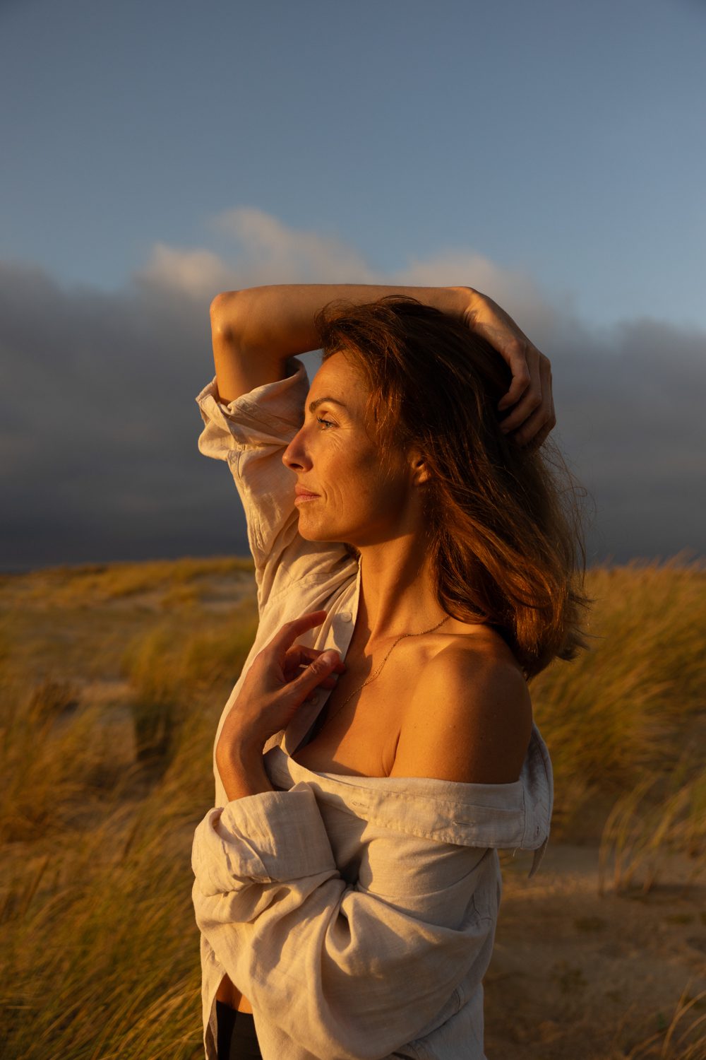 Femme debout dans les dunes au coucher du soleil, bras levé