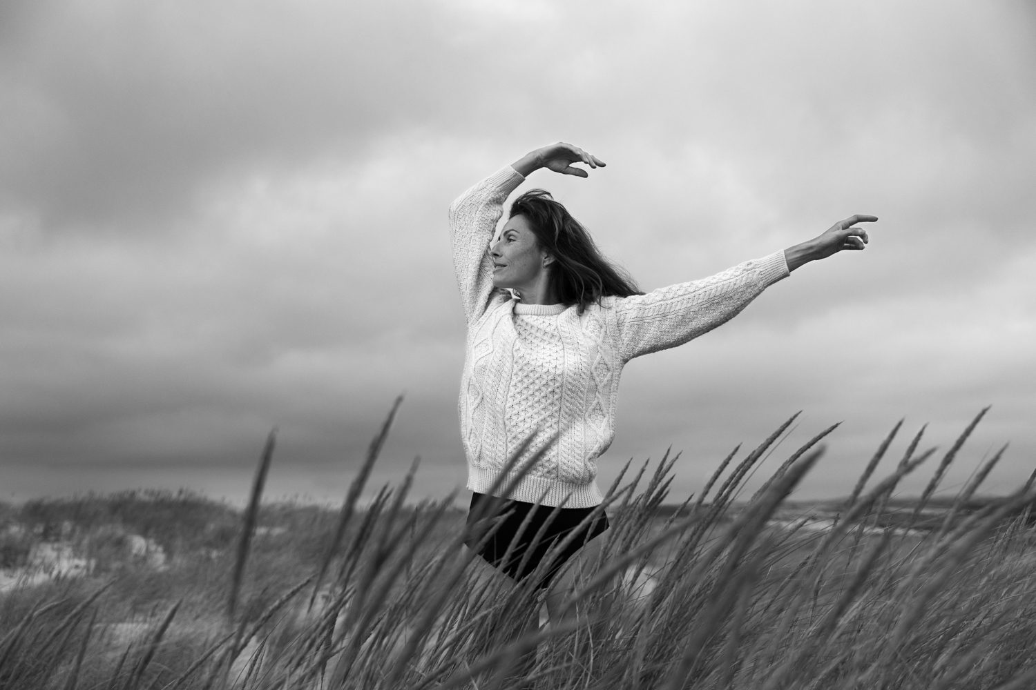 Femme debout dans les dunes, bras levé, en noir et blanc