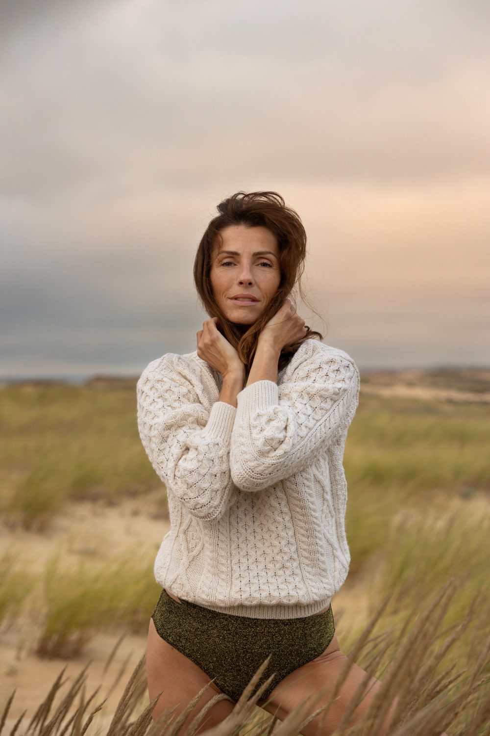 Femme debout dans les dunes, bras croisés, regard face caméra