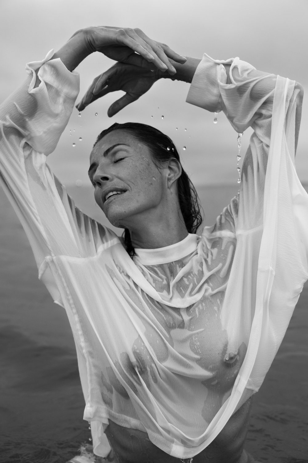 Femme debout dans l’eau, bras levés, vêtement transparent