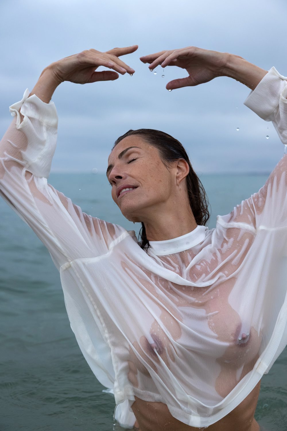 Femme debout dans l’eau, bras levés, vêtement transparent