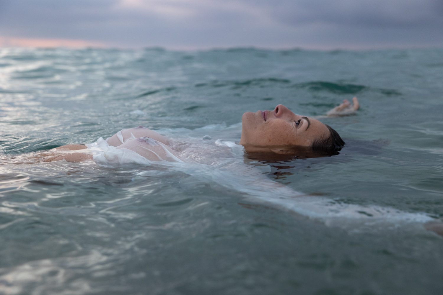 Femme allongée sur l’eau, bras ouverts, mer calme