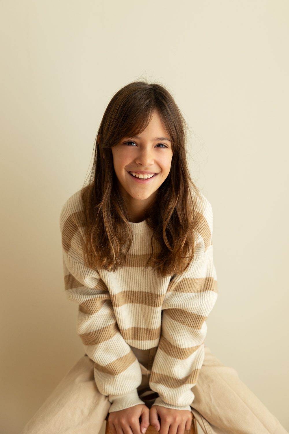 Fille souriante assise, pull rayé, fond clair